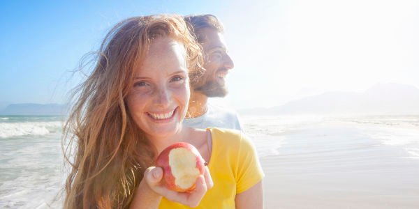 Smiling couple on sunny beach, with woman holding an apple